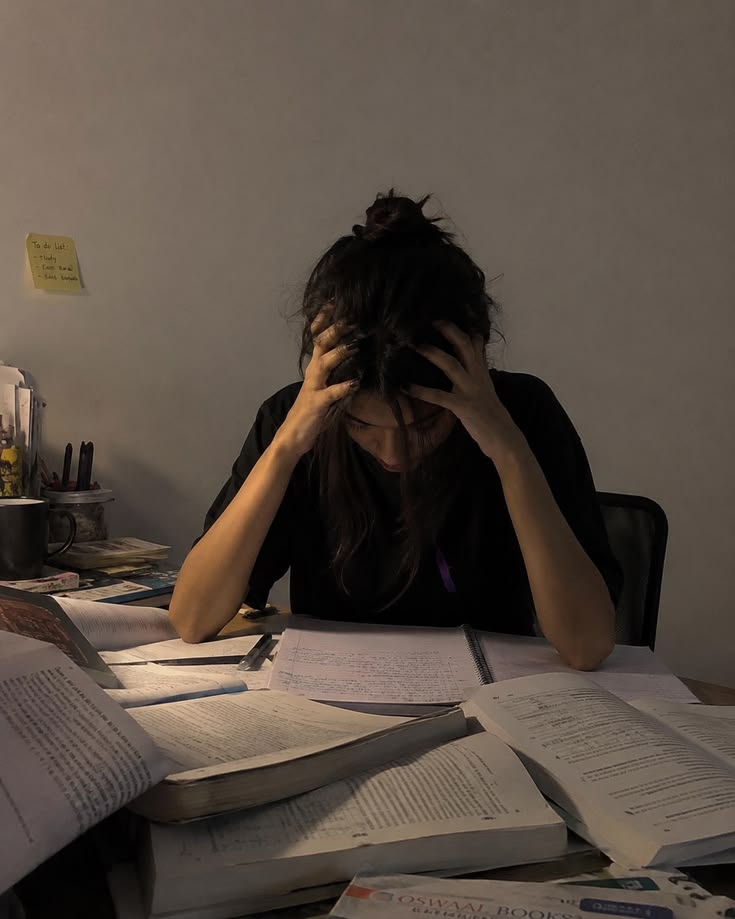 Student overwhelmed at a desk covered in books